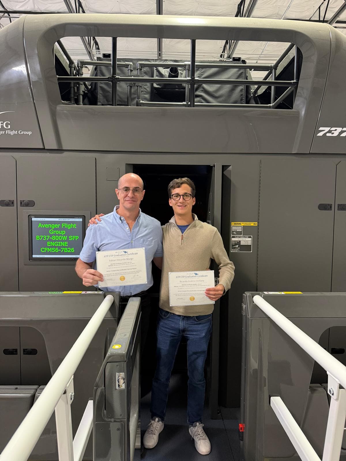 Two AVS graduates holding ATP-CTP certificates in front of the B737-800W simulator